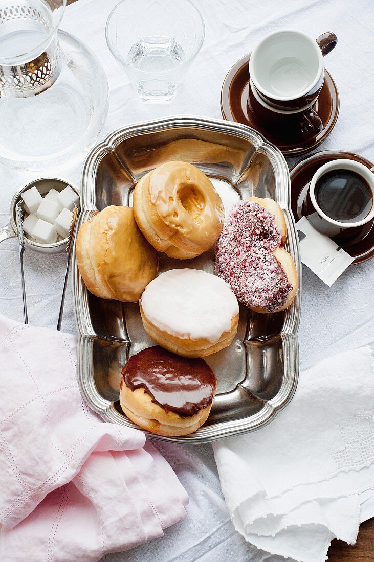 Assorted doughnuts on a tray with coffee cups to one side