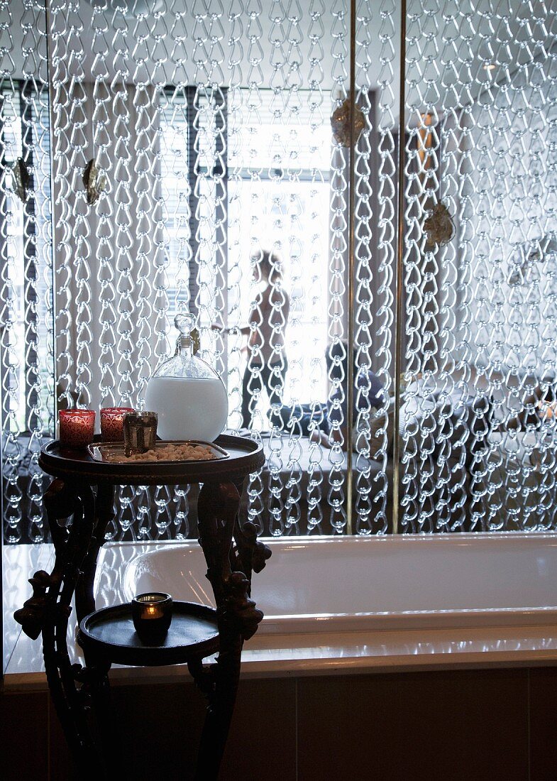 Chain curtain screening bathtub from bedroom; toiletries on carved wooden table