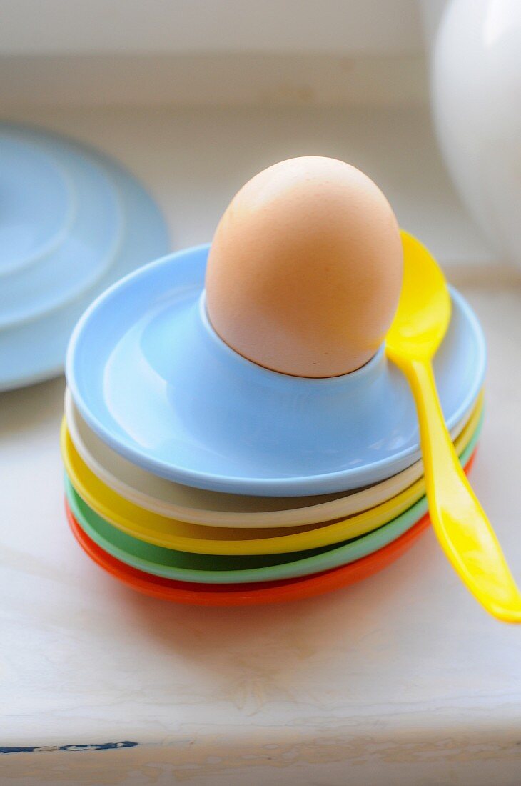 Bunte Eierbecher aus Plastik und ein Frühstücksei mit Löffel