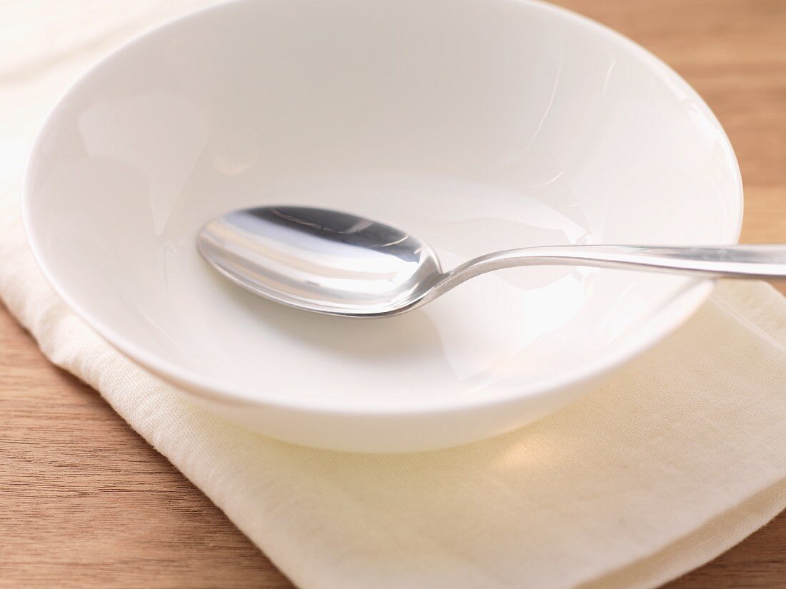 An empty white soup bowl with a spoon