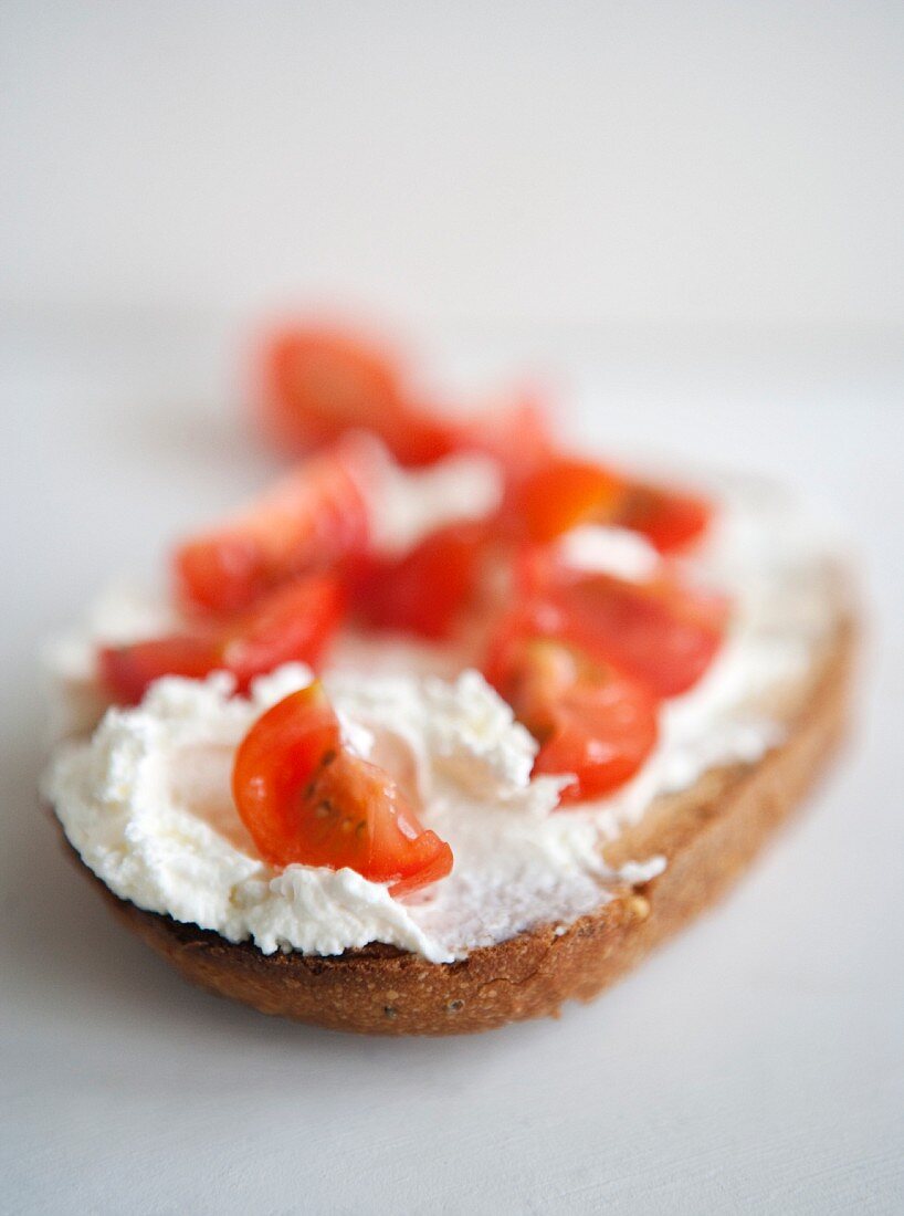 A slice of bread topped with cream cheese and tomatoes