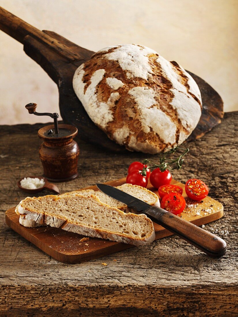 Classic sourdough rye-wheat bread: a whole loaf and slices of bread with cherry tomatoes on a chopping board
