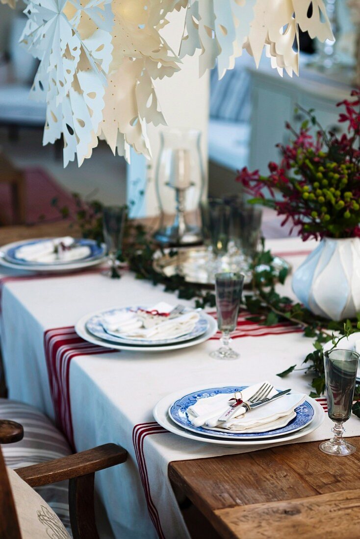 Country-house-style table festively set for Christmas with red and white striped tablecloth and artistic, white paper Advent stars