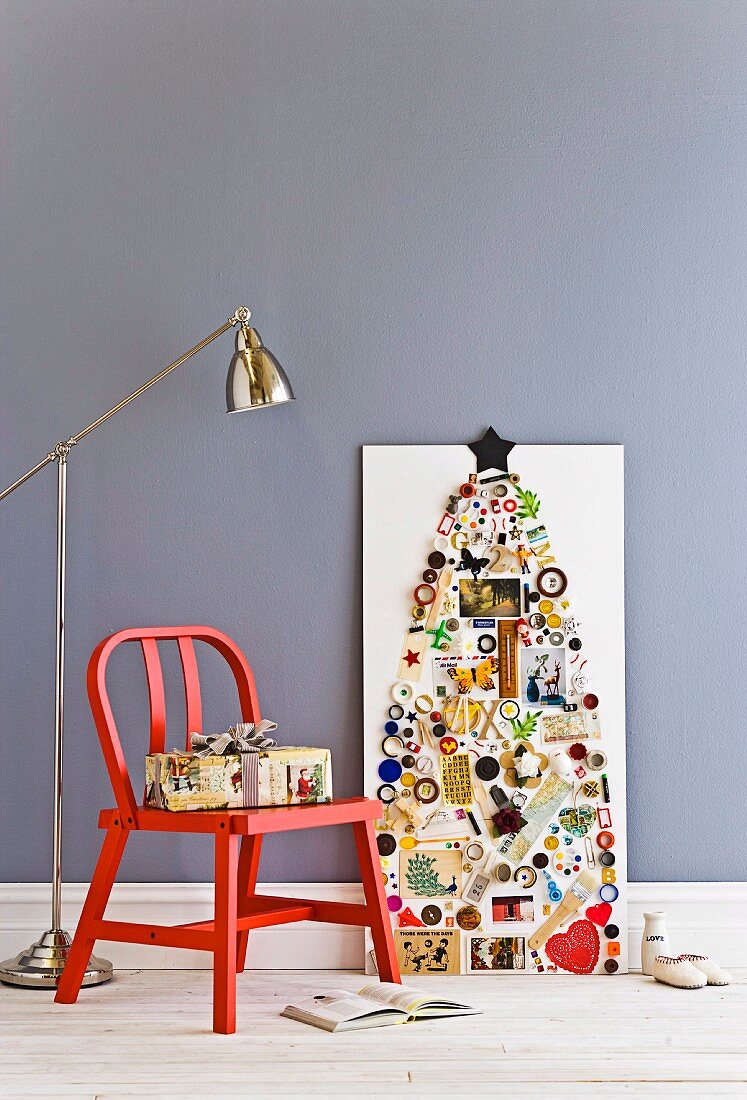 Stylised Christmas tree collage on white plywood panel; wrapped present on red wooden chair and industrial-style standard lamp