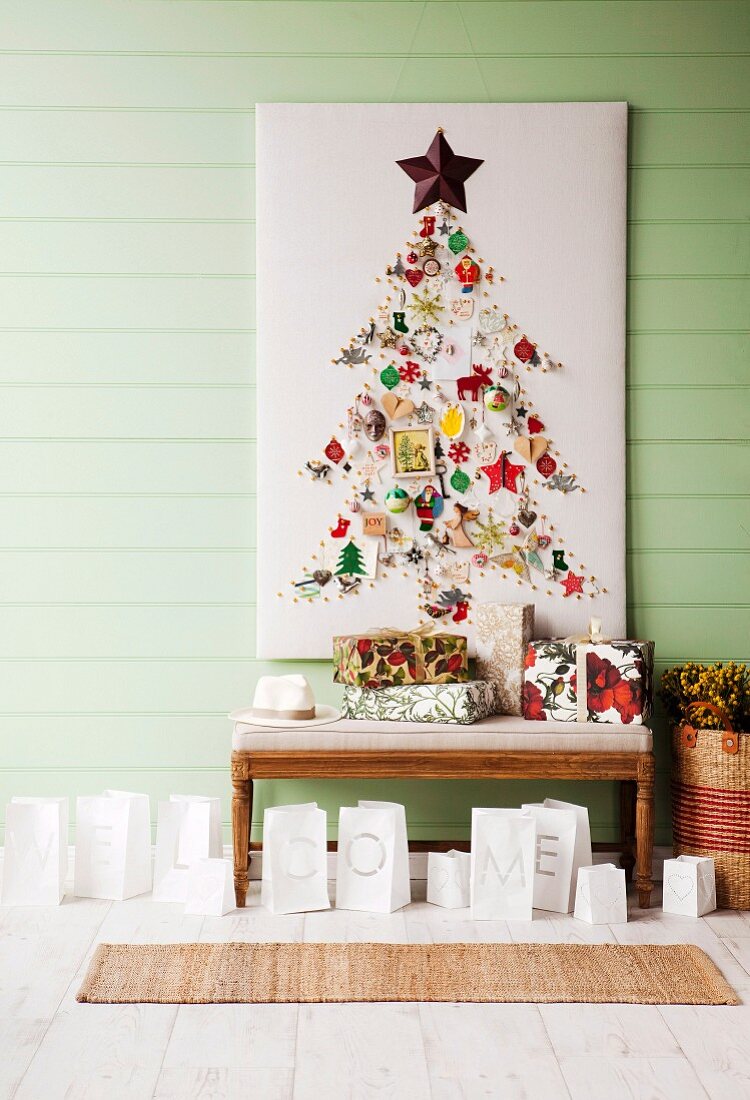 Christmas tree decorations arranged in shape of Christmas tree on white panel above presents and paper bags used as tealight holders