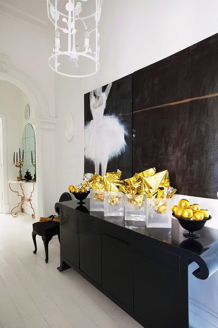 Gold Christmas decorations on black postmodern sideboard and modern painting of ballerina in elegant entrance hall