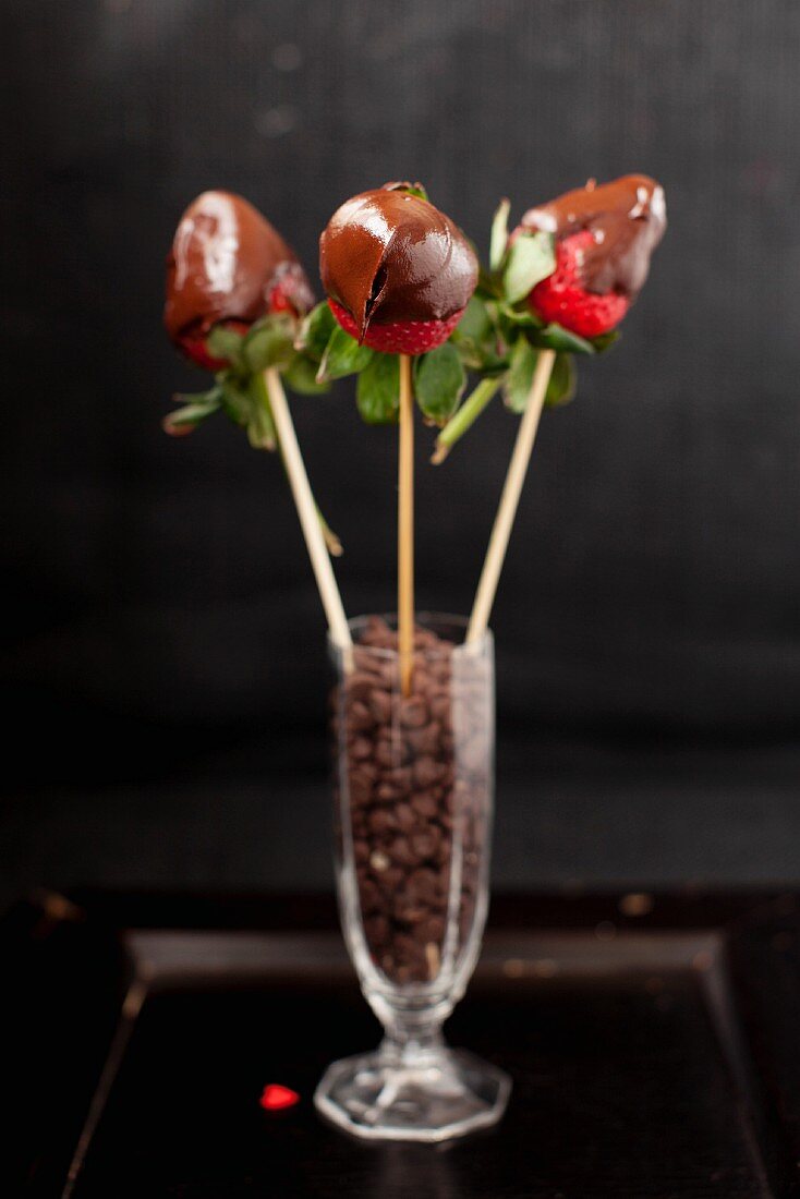 Drei Schokoladenerdbeeren auf Spiessen in einem Glas mit Chocolatechips