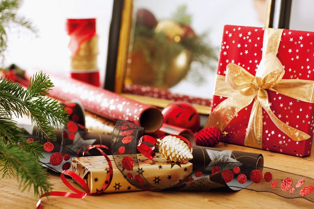 Geschenkpapierrollen und Bänder neben Weihnachtspäckchen mit Schleife