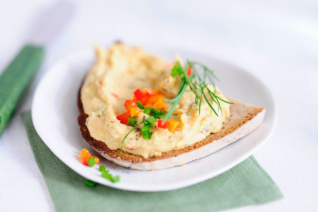 Black bread topped with tofu spread, garnished with cubes of pepper