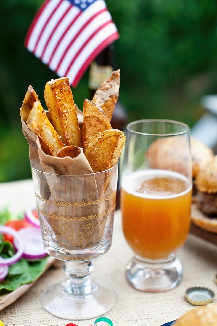 Potato Wedges auf einem Tisch im Freien, im Hintergrund büffel-Burger und US-Fahne