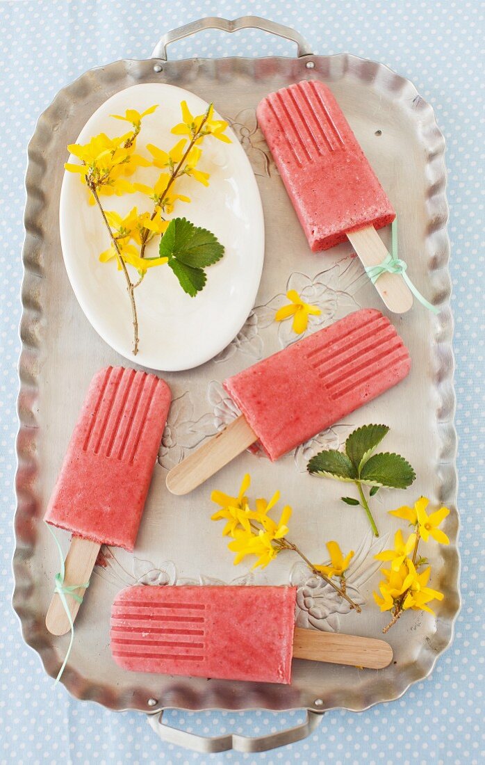 Erdbeer-Smoothie-Eis am Stiel auf einem Tablett mit Forsythien-Blüten