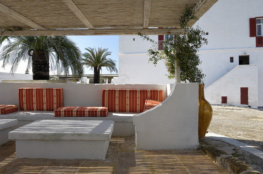 Überdachte Terrasse mit gemauerten Möbeln und weichen Sitz- und Liegepolstern