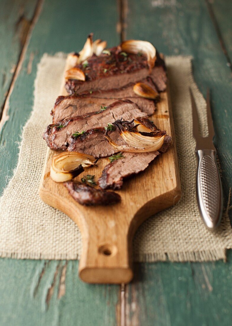 Gebratenes Flank Steak mit Pilzen, Zwiebeln, Knoblauch und Thymian auf einem Schneidebrett