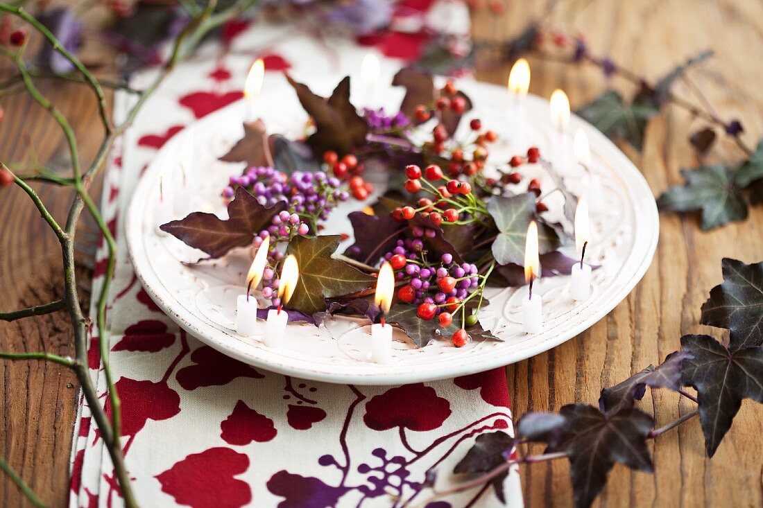 Wreath of callicarpa, tiny rosehips and purple ivy surrounded by small candles on plate