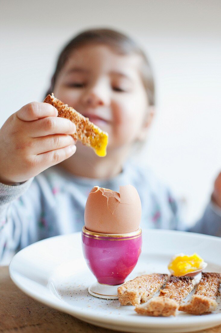 A girl dipping a toast soldier in a soft-boiled egg