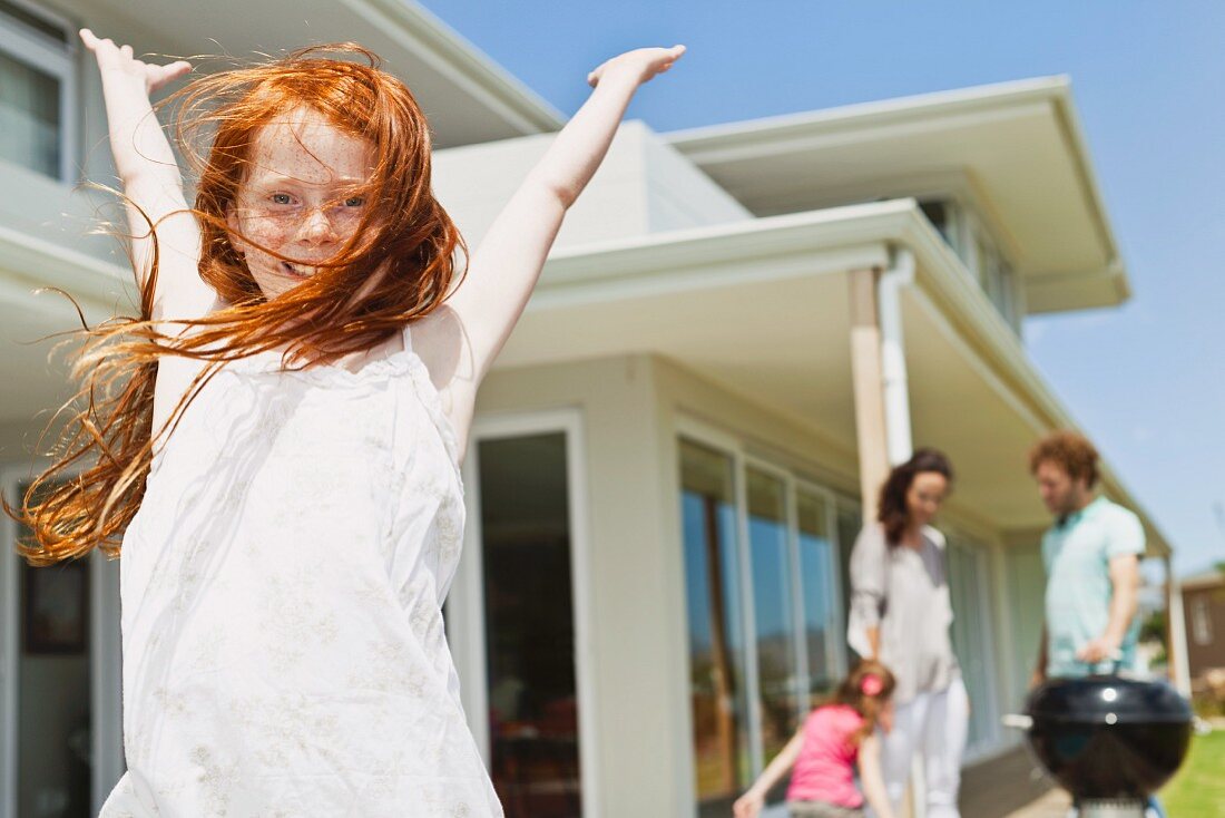 Joyful girl in the front garden, family barbecuing