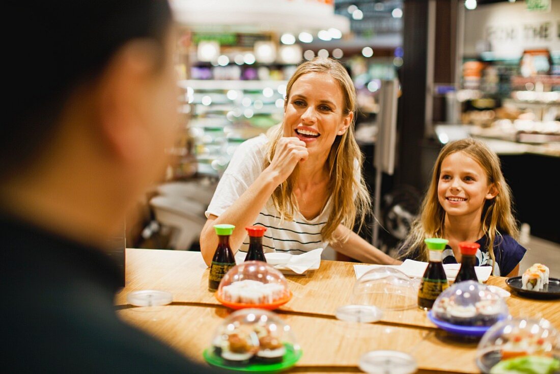 A mother and daughter eating sushi in a gourmet food shop