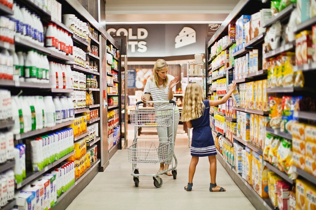 Woman and a young girl with a shopping trolley walking down a supermarket aisle