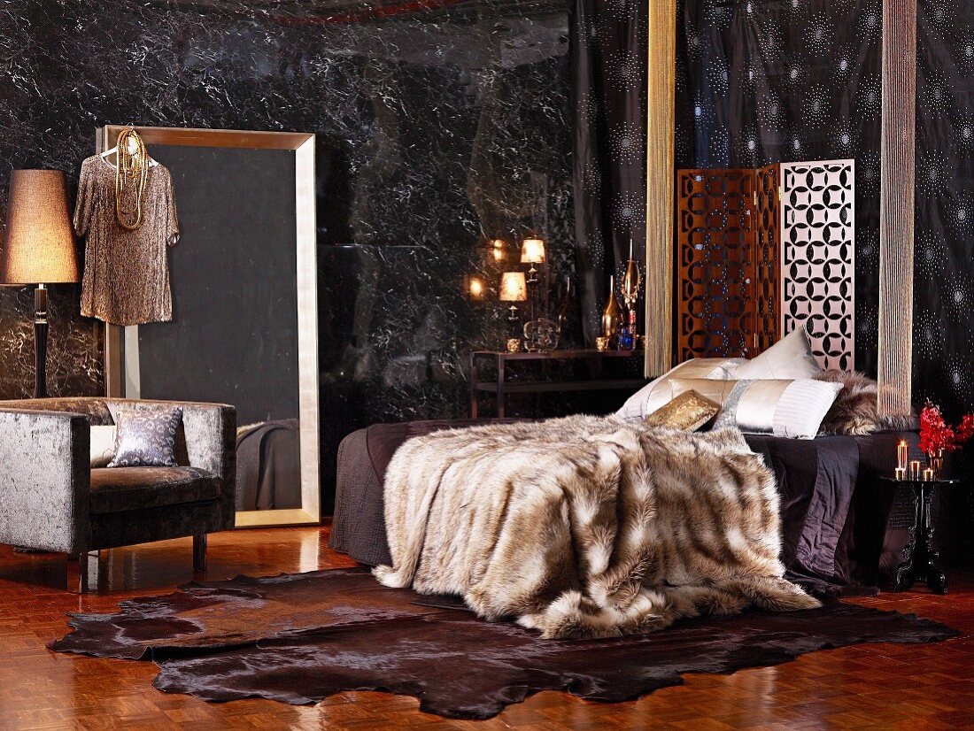 Schlafzimmer mit Felldecken und Edelholzparkett, großem Wandspiegel und edlen Stoffen