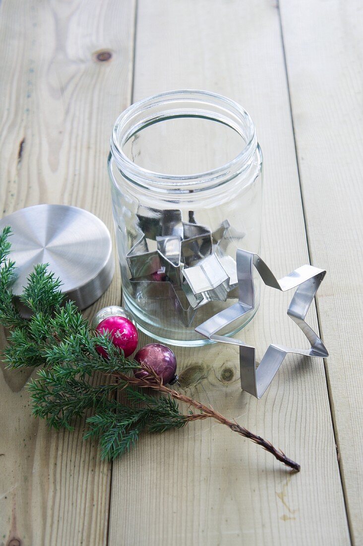 Sternausstecher in einem Schraubglas, daneben Koniferenzweig und Weihnachtsschmuck