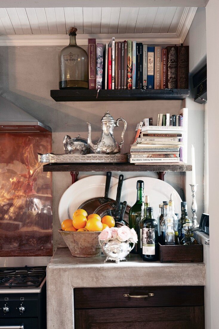 Cookery books and bottles on floating shelves & crockery on cast concrete base unit in kitchen