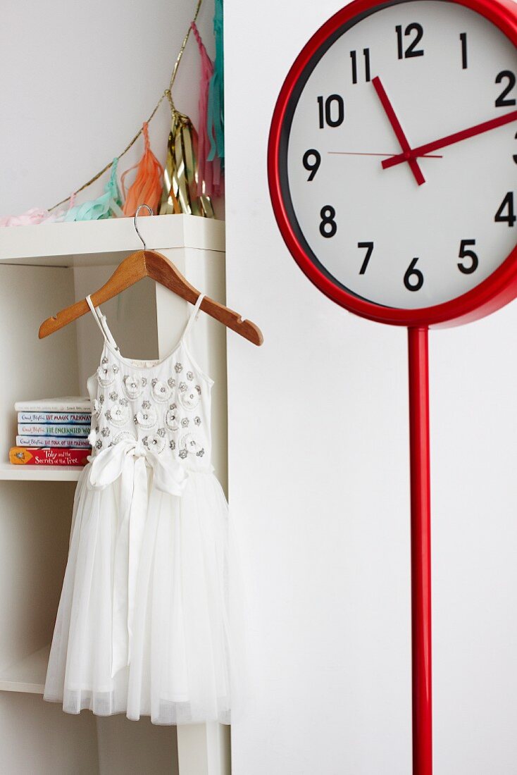 White tulle dress on wooden clothes hanger and red station clock in girl's bedroom