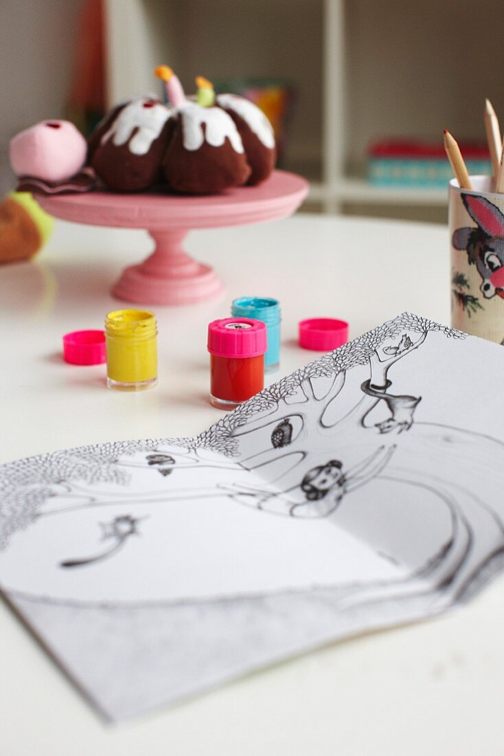 Farbtöpfchen und Ausmalbuch auf Tisch in Kinderzimmer; Deko Kuchen auf Plastik Etagere