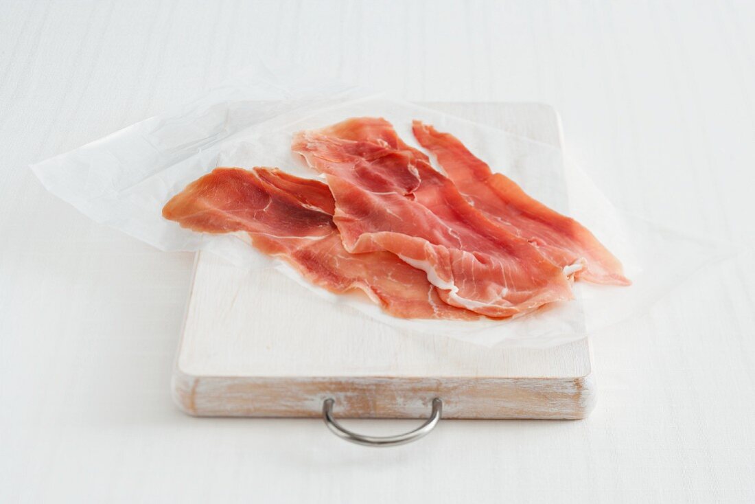 Wafer-thin sliced dry-cured ham on paper on a wooden board