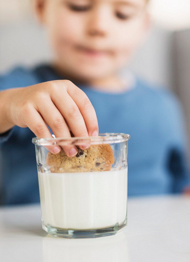 Kleiner Junge taucht Plätzchen in ein Glas Milch