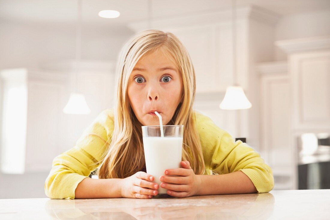 Blondes Mädchen trinkt Milch mit Strohhalm