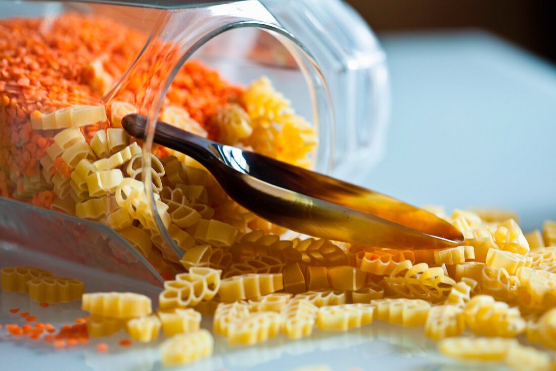 Dried pasta and red lentils in an overturned storage jar with a scoop