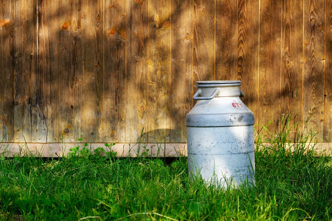 A milk churn in the grass outside a wooden cabin