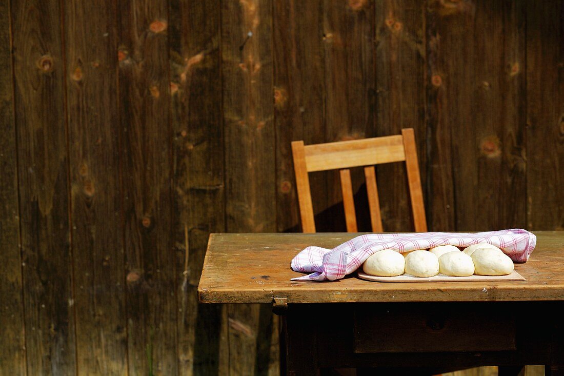 Hefeteigkugeln mit Küchentuch abgedeckt auf Holztisch vor Holzhütte