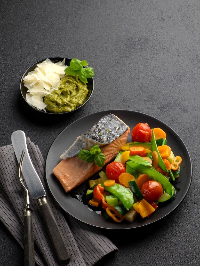 Salmon fillet with colourful vegetables on a black plate, with pesto