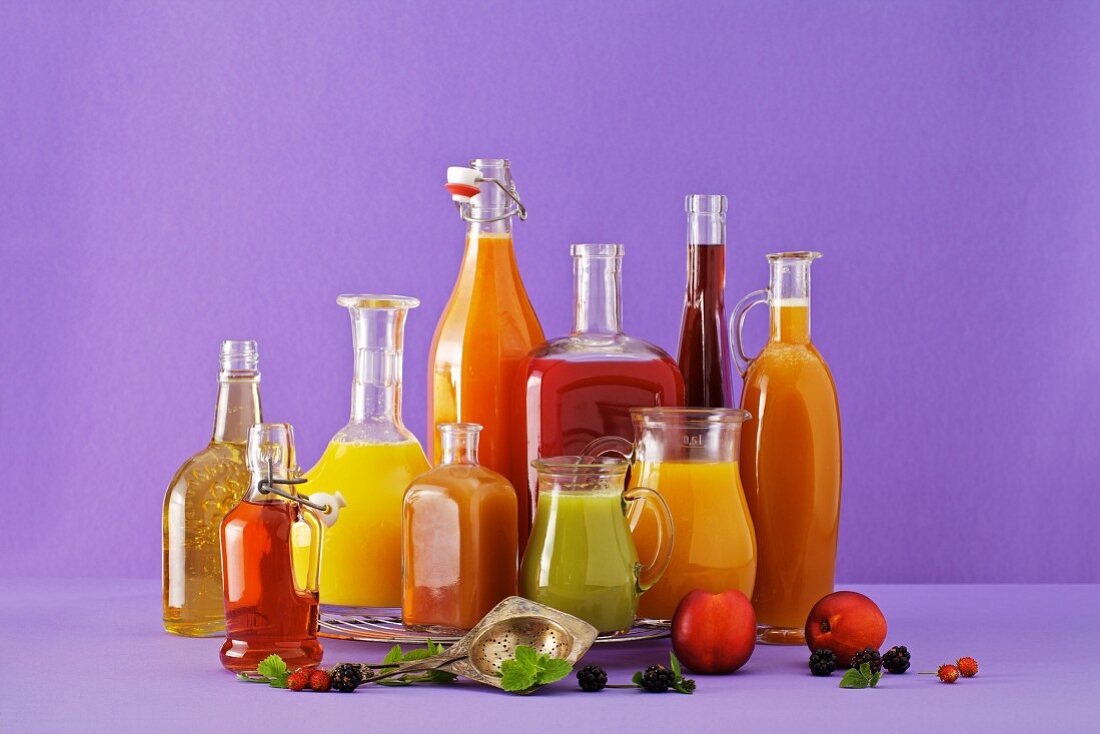 Freshly squeezed fruit juices in assorted glass containers against a purple background