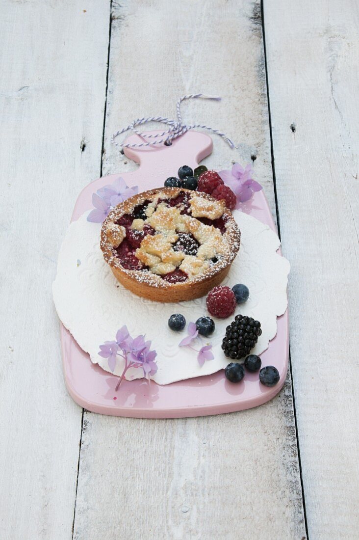 Individual berry tart with buttery crumble on a pink board