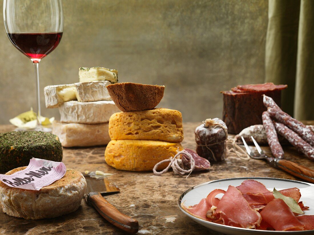 A still life featuring cheese, sausage and red wine from France