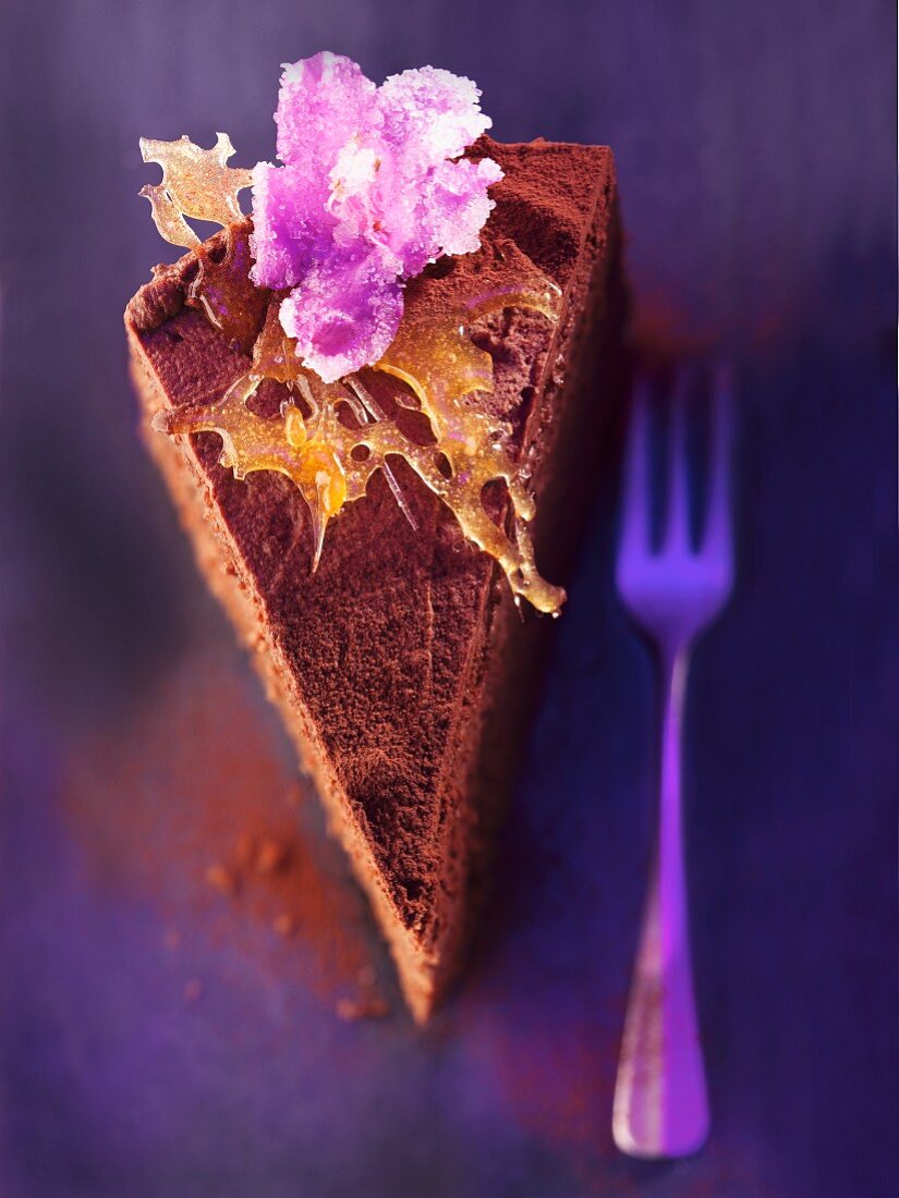 A slice of chocolate layer cake with caramel and candied flowers