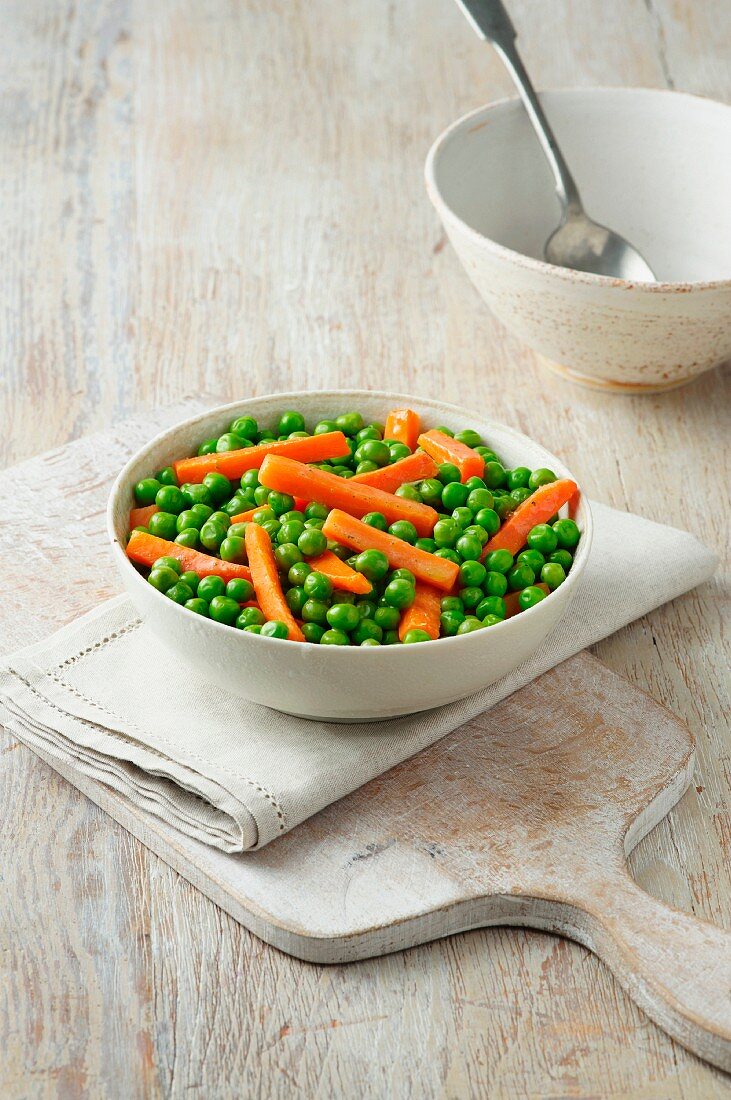 Peas and carrots in white bowl on cream cotton cloth