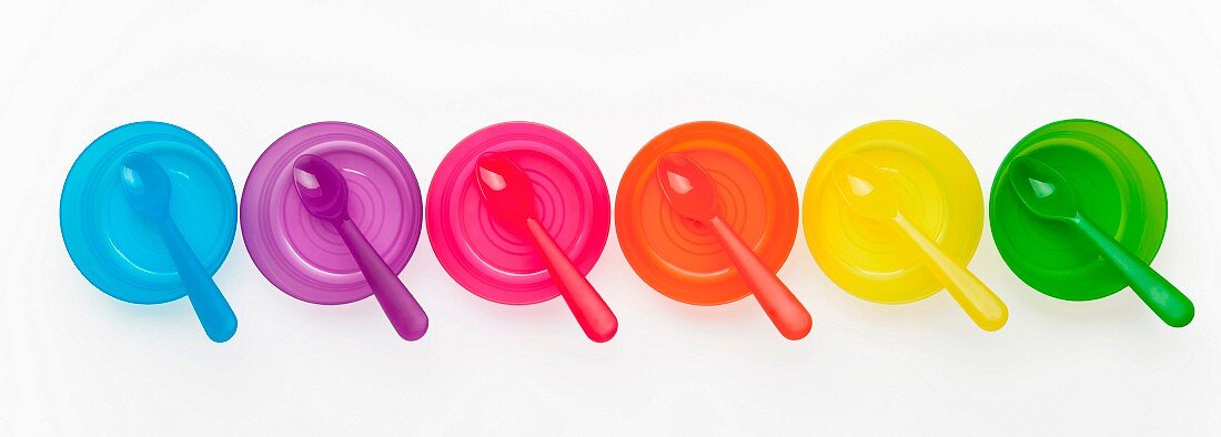 Colourful plastic spoons and bowls in a row