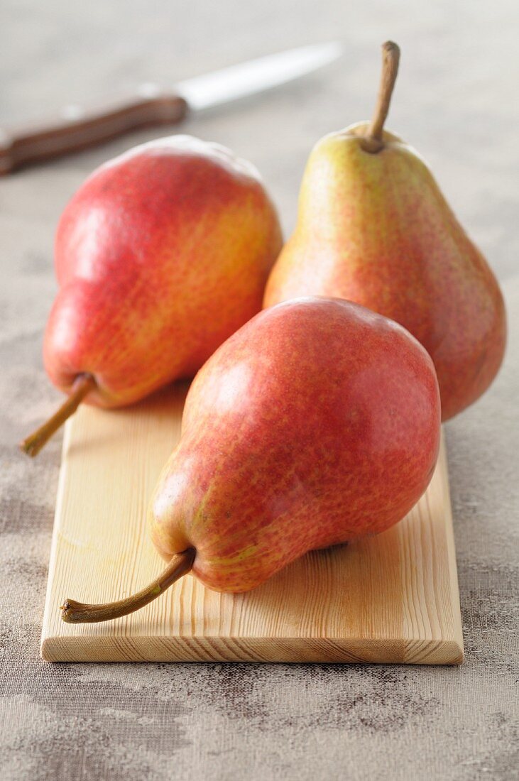Three red pears on a small wooden board