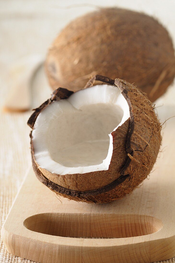 A whole coconut and one broken open, on a wooden board