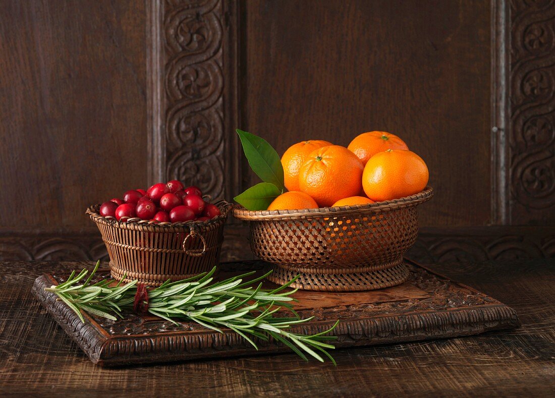 Ingredients to create Clementine and Cranberry Lamb Rack. Clementines in woven wooden bowl, cranberries in small wooden bowl and sprigs of rosemary