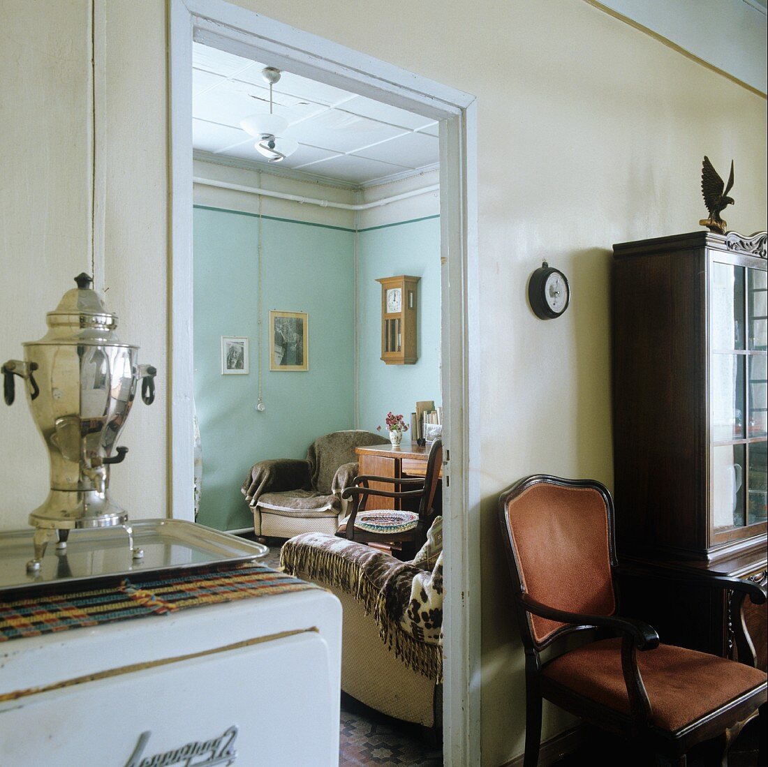 Open doorway with view into living room flanked by samovar on kitchen cupboard and antique armchair in dining room