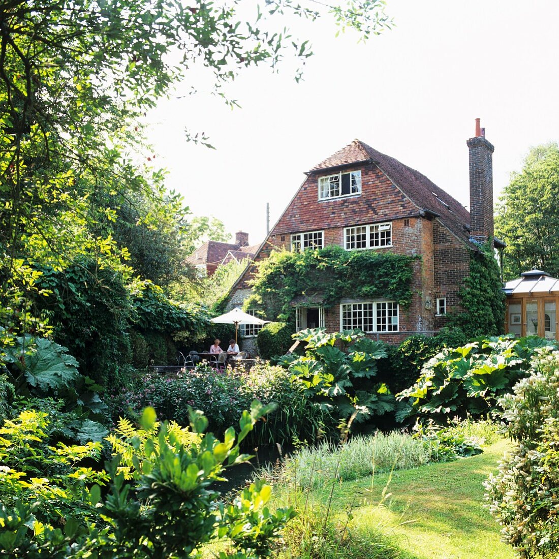 Sommerlicher Garten und ehemalige Mühle als Wohnhaus mit berankter Fassade