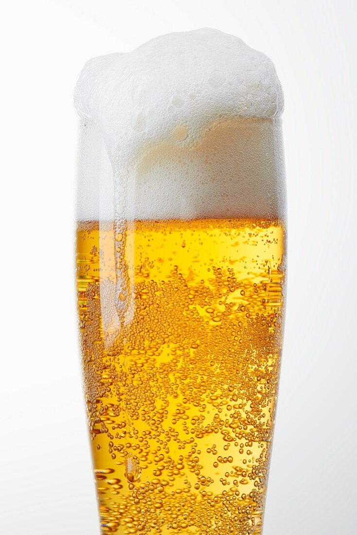 A glass of light beer with overflowing beer foam