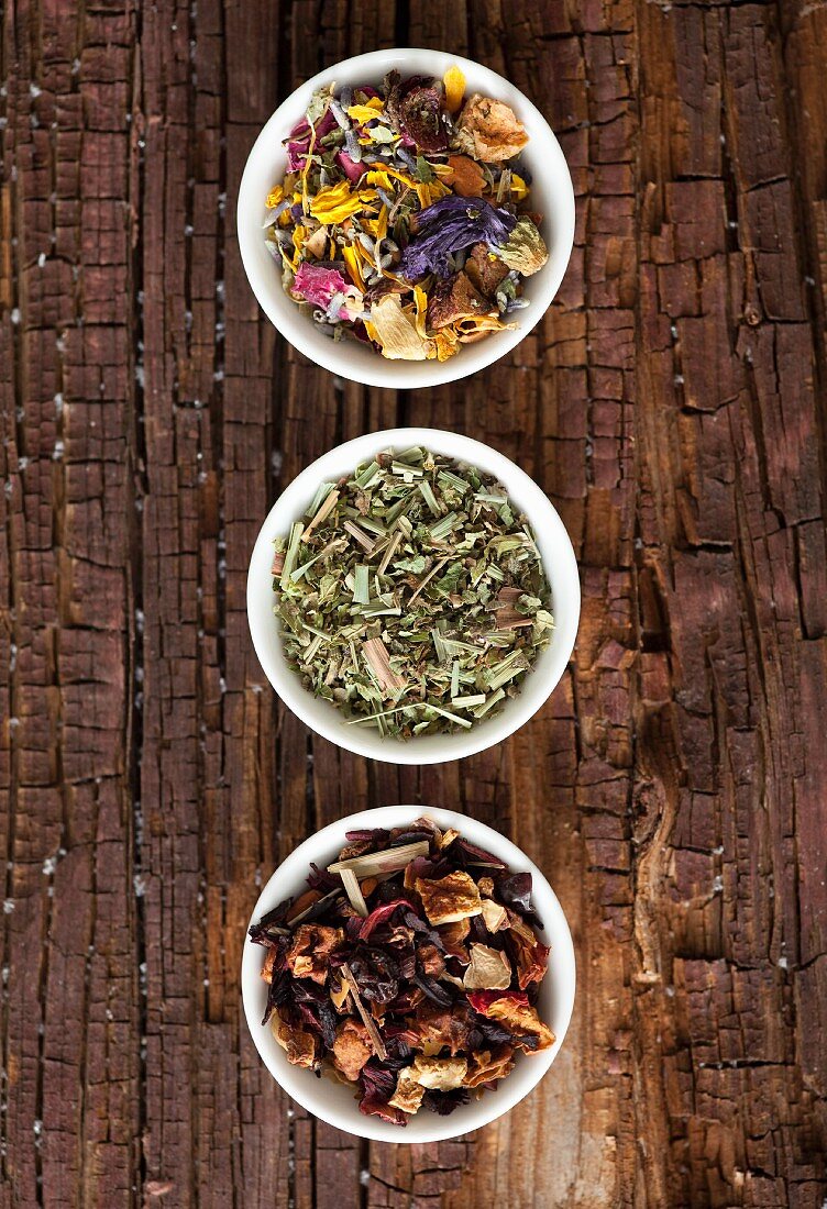 Assorted tea blends in small bowls on a rustic wooden surface
