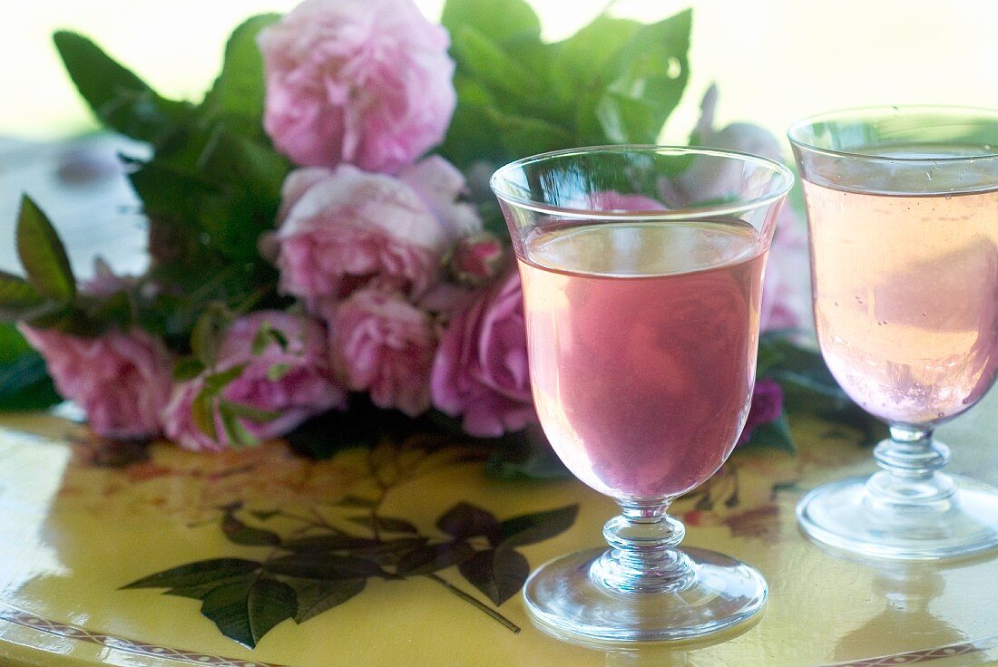 Rosensirup in zwei Gläsern, im Hintergrund Rosenstrauss