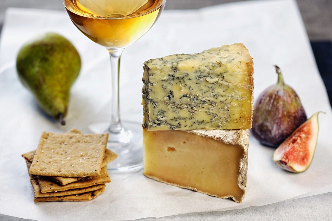 Assorted types of cheese with figs, a pear, crackers and a glass of white wine