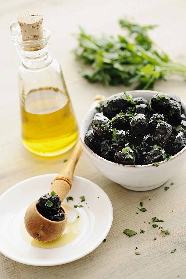 Schwarze Oliven in einer Schale mit Petersilie und Olivenöl